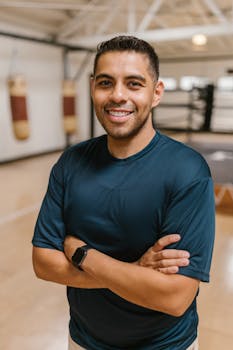 Portrait of a cheerful man with arms crossed in a gym, wearing a blue shirt.
