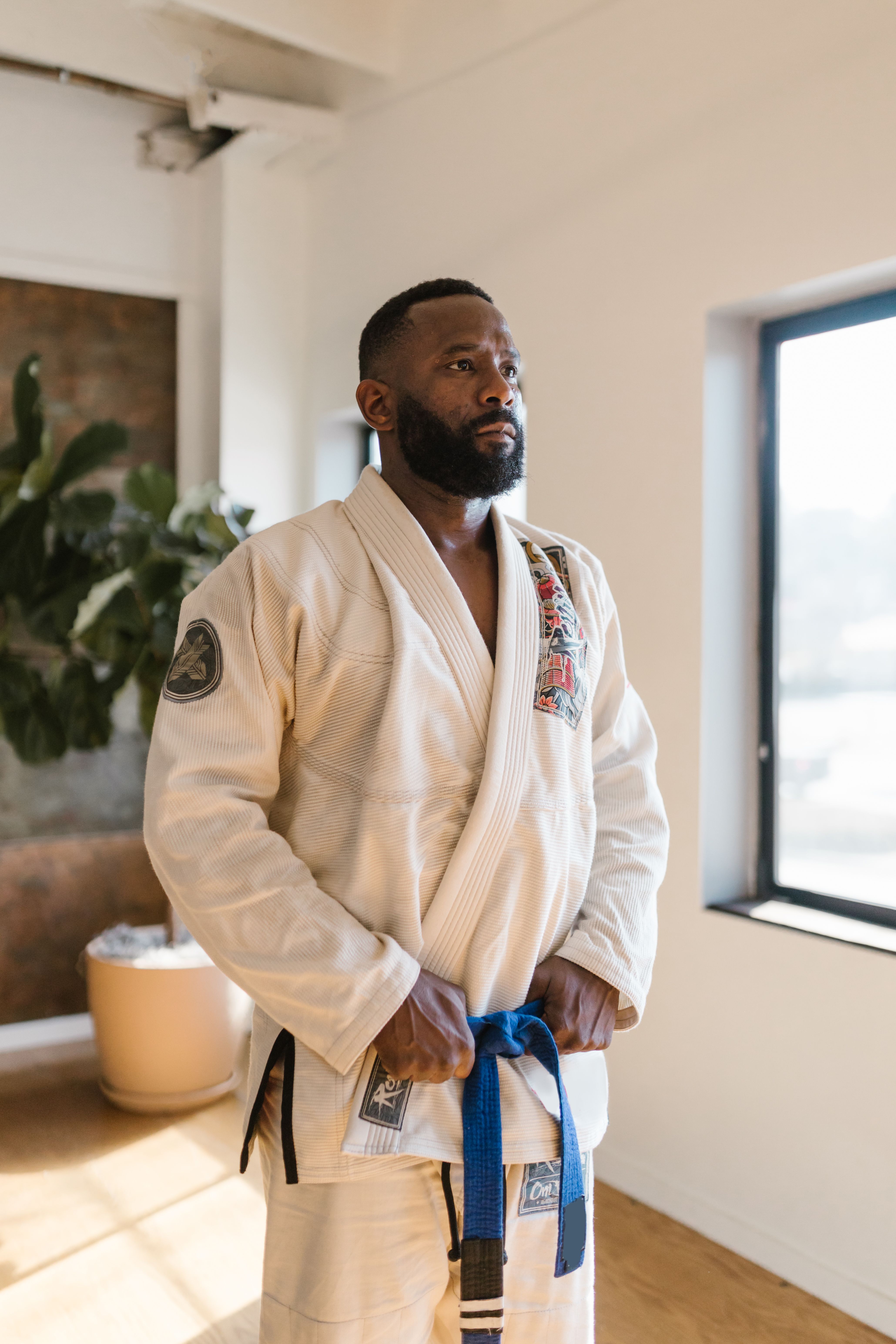 Adult male in a martial arts gi prepares for practice in a sunny indoor setting, standing confidently.