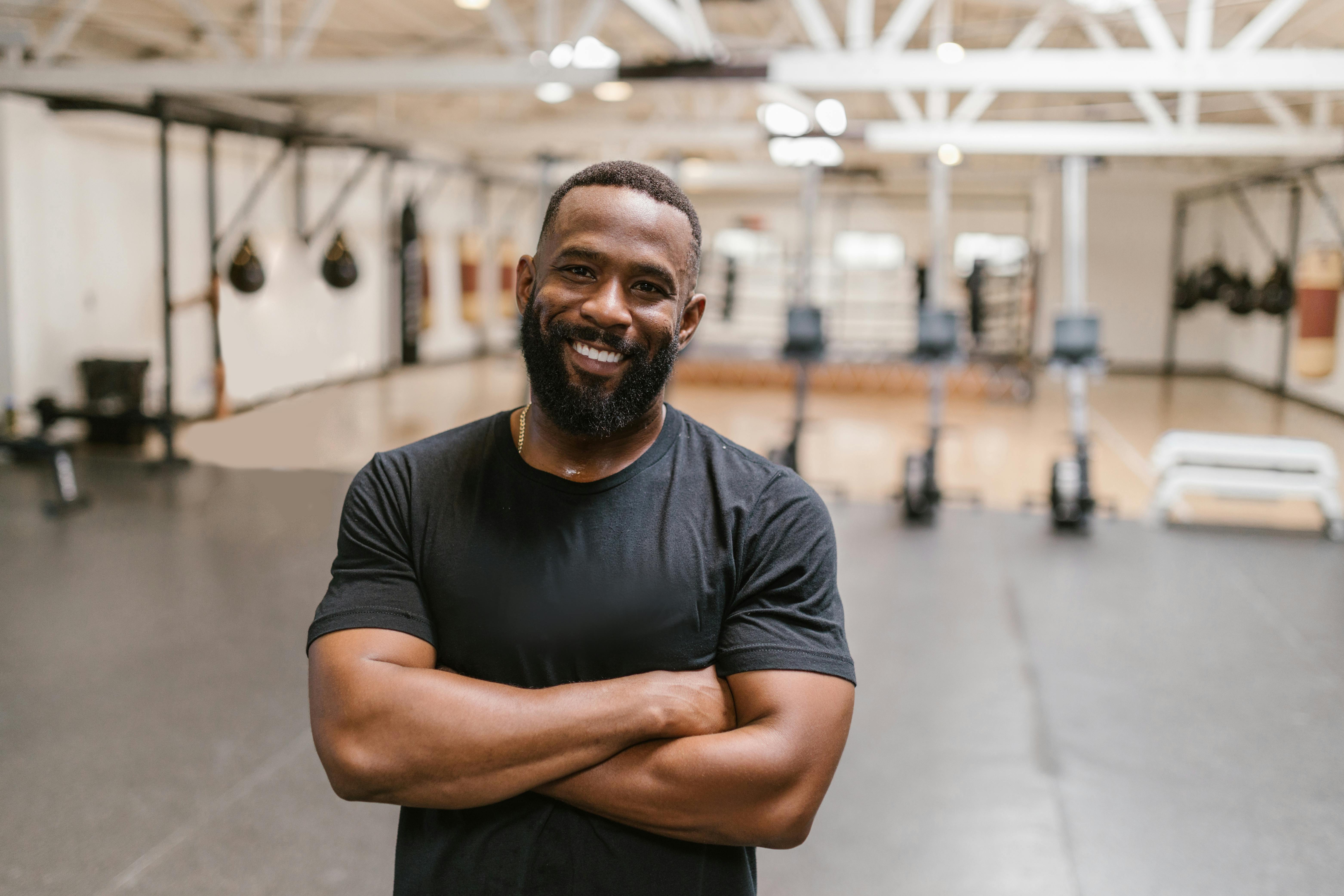 Smiling man with beard and arms crossed in a gym. Ideal for lifestyle and fitness themes.