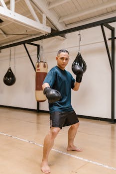 Focused young athlete practicing boxing in an indoor gym setting, wearing gloves and ready to fight.