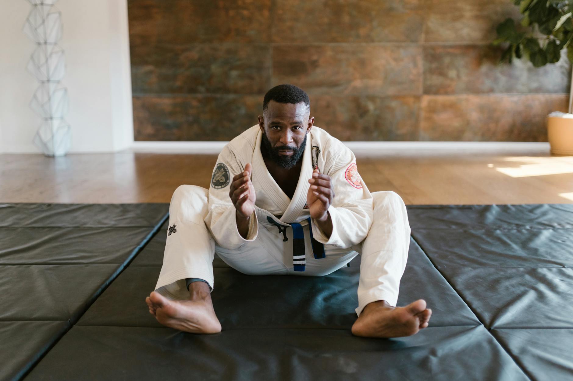 Martial artist wearing a gi sits on a mat, ready for training indoors.