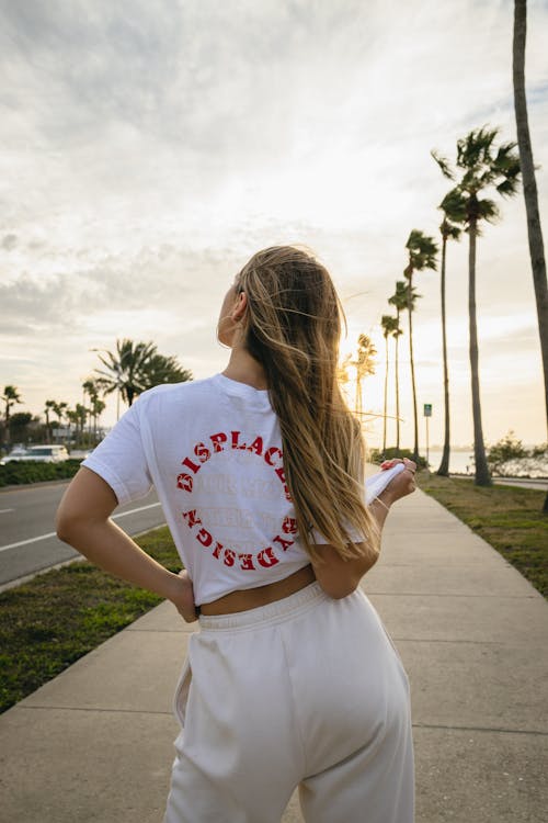 Blonde Woman in T-shirt Standing near Palm Trees at Sunset