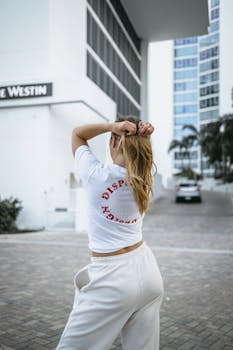 A woman adjusts her hair in an urban setting, highlighting modern architecture.
