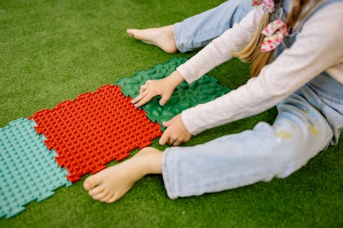 Girl in White Long Sleeve Shirt Playing With Plastic Mats On Green Carpet