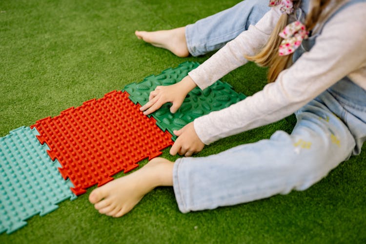 Girl In White Long Sleeve Shirt Playing With Plastic Mats On Green Carpet