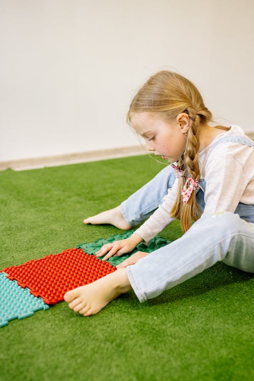 Free Girl in White Long Sleeve Shirt Playing With Mats On Green Carpet Stock Photo