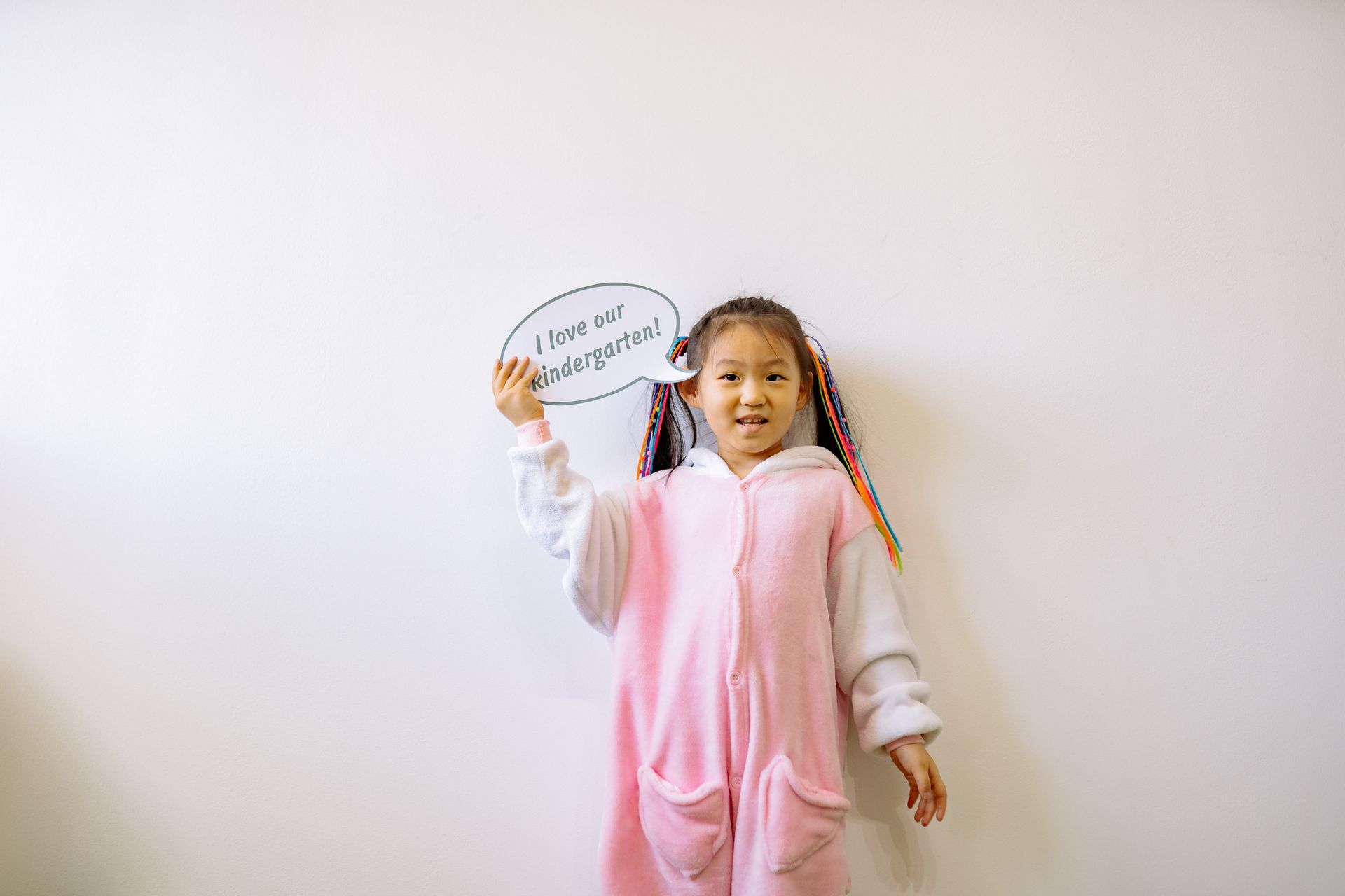 A happy child in a vibrant costume holds a sign expressing love for kindergarten.