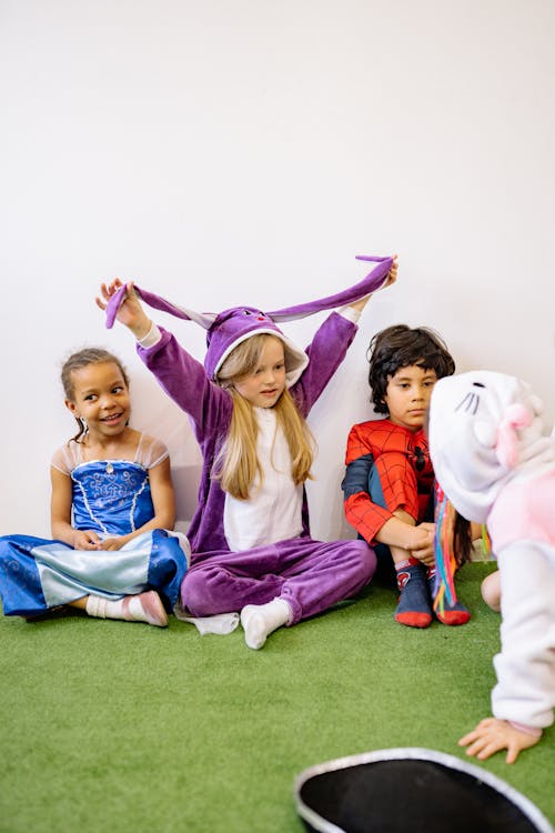 Children Wearing Different Costumes Sitting On Green Carpet
