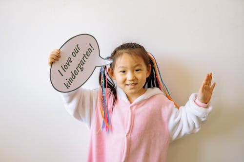 Girl in Pink and White Overall Holding A Cardboard With Text