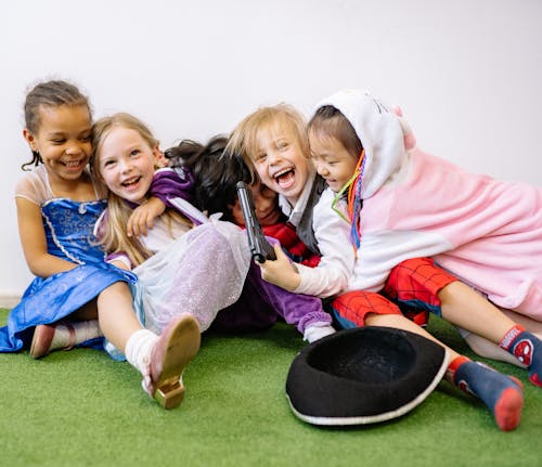 Children Having Fun While Sitting on Green Carpet Wearing Different Costumes