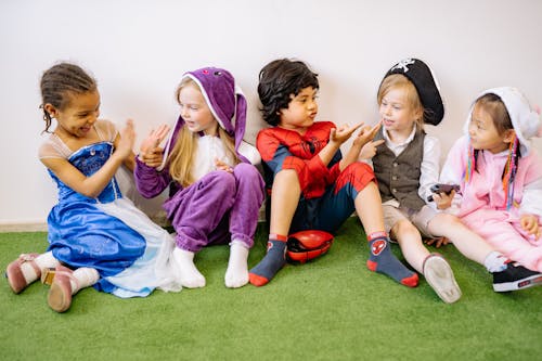 Free Group Of Children Sitting On Green Carpet Wearing Different Costumes Stock Photo