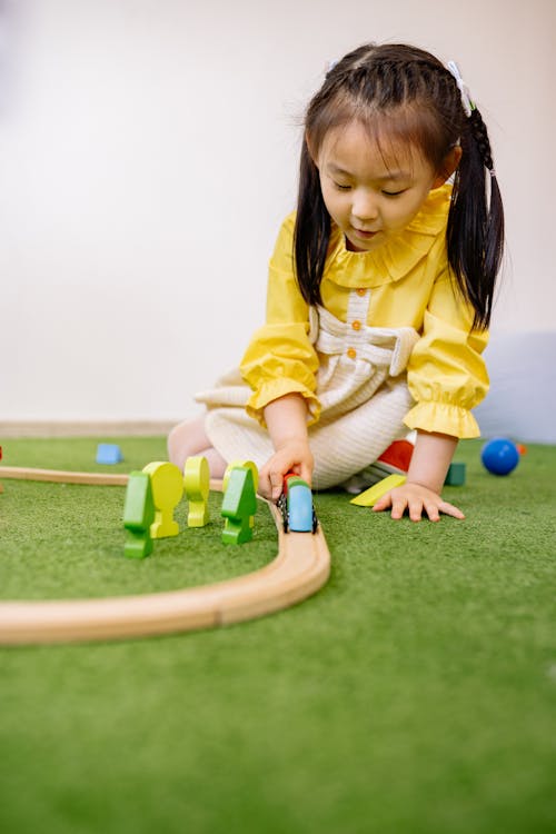 Free Girl in Yellow Dress Playing With Wooden Toy Cars Stock Photo