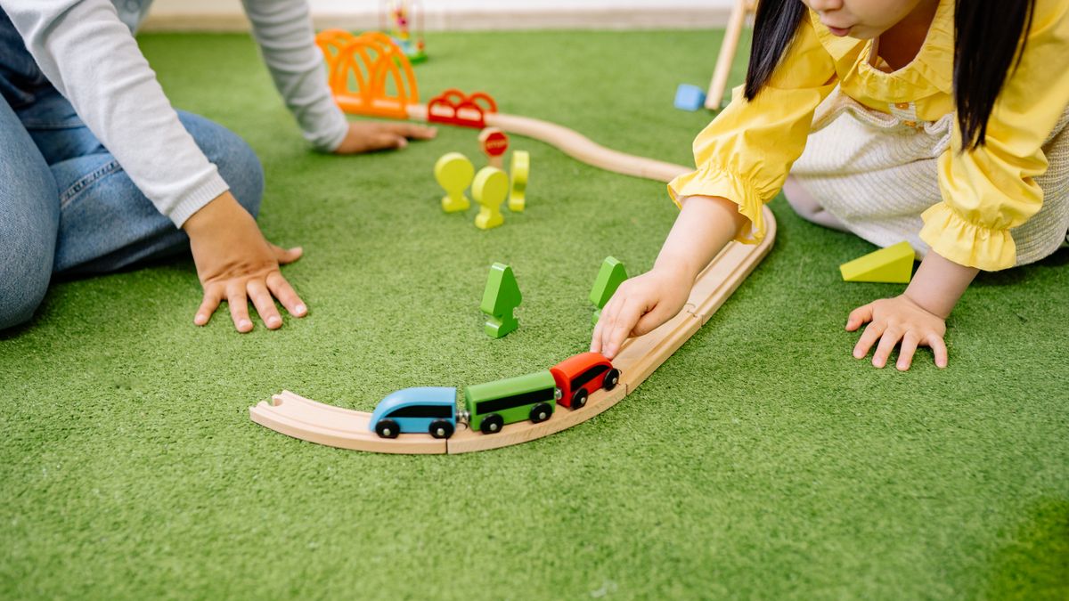 Young girl enjoying playtime with a wooden toy train indoors.