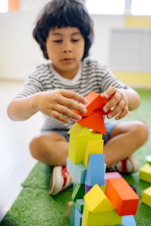 Boy in White and Black Stripe Shirt Playing With Wooden Blocks