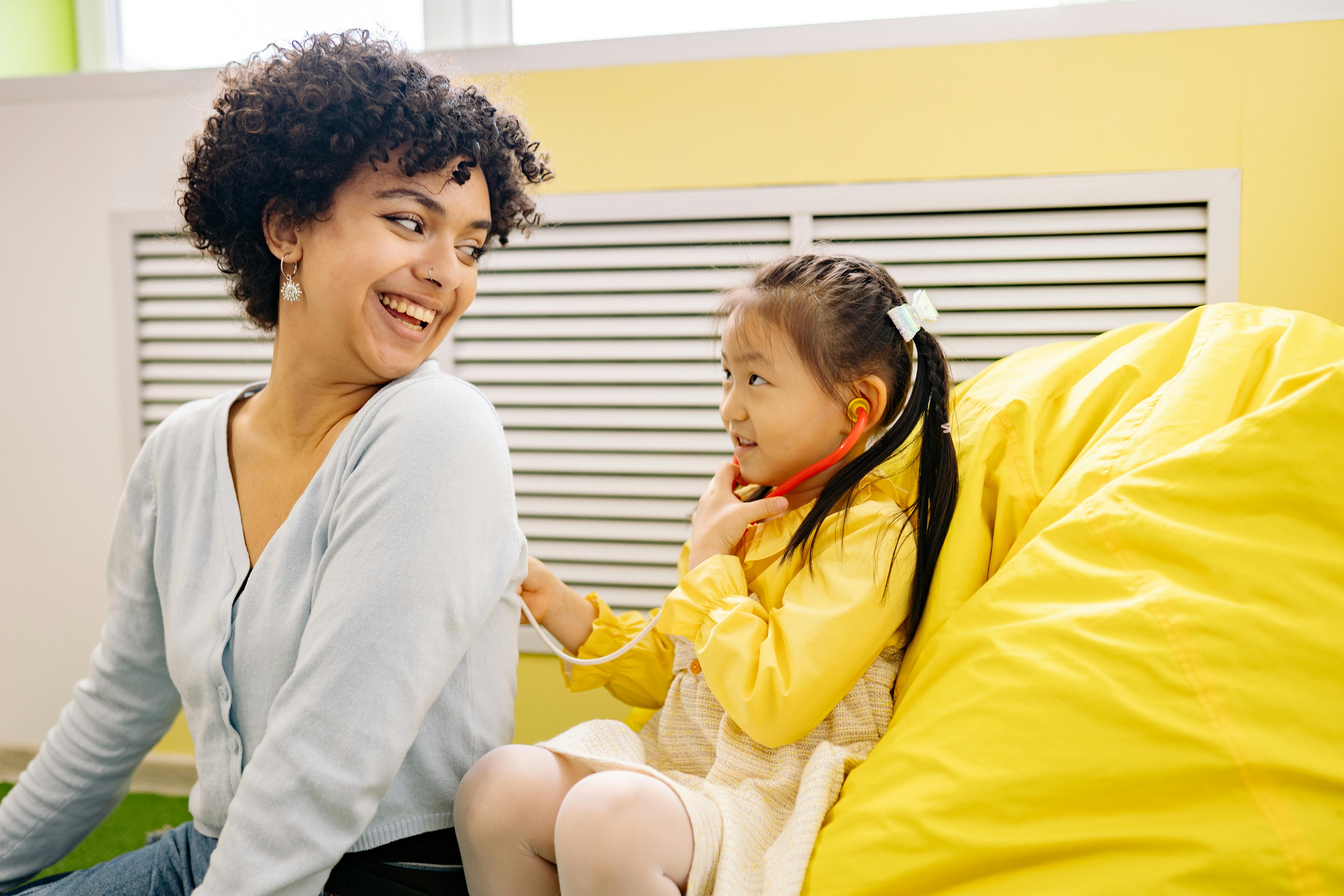 woman with curly hair playing with little girl doctor