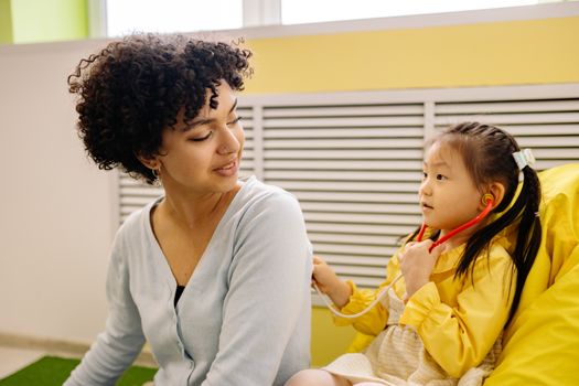 Child plays pretend doctor with stethoscope and adult, fostering imagination indoors.