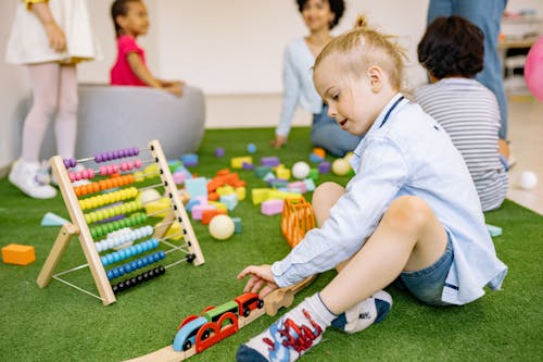 Boy in Blue Long Sleeve Shirt and Denim Shorts Playing With Wooden Toy Cars