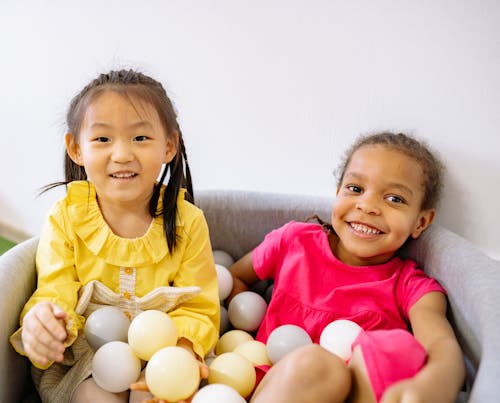 Pretty Little Girls Sitting Inside A Tub With Plastic Balls