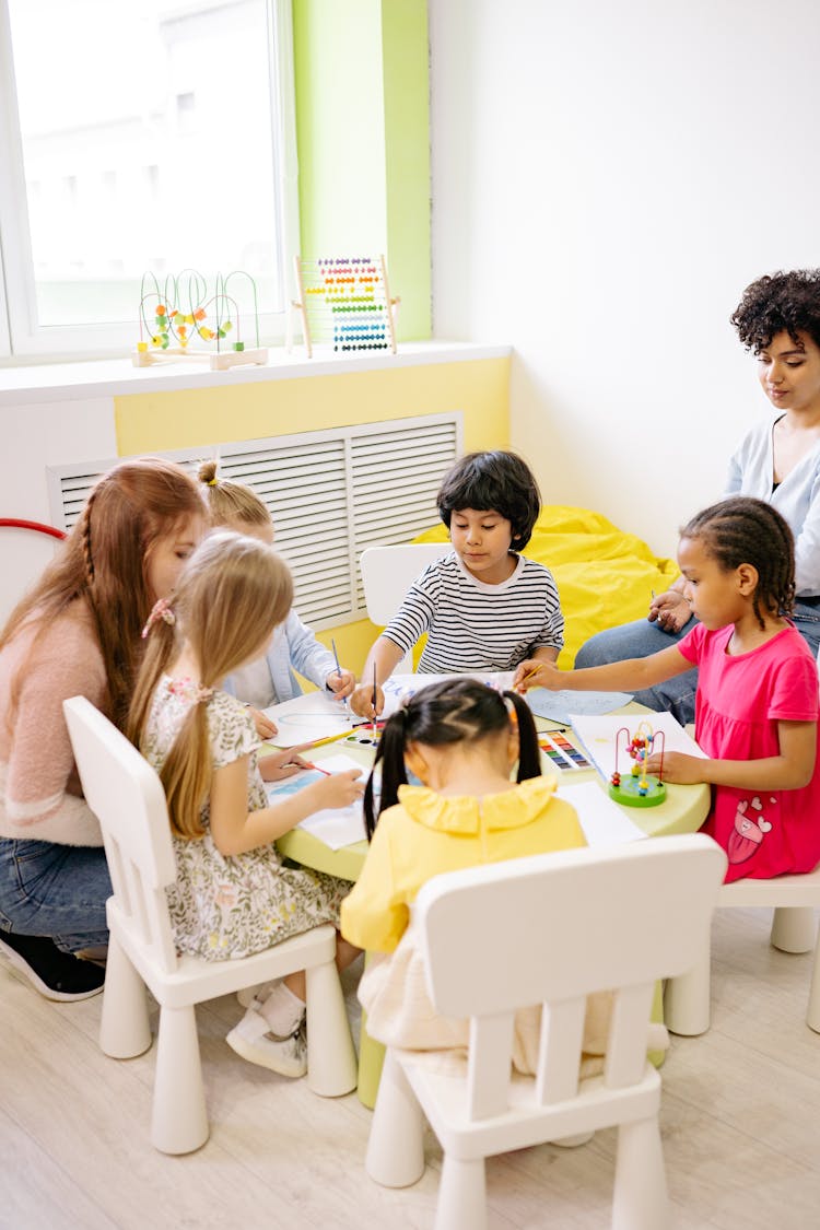 Group Of Children Sitting Around A Table And Doing Art