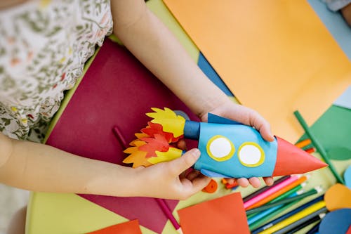 A Child Holding A Jet Made From Colored Papers