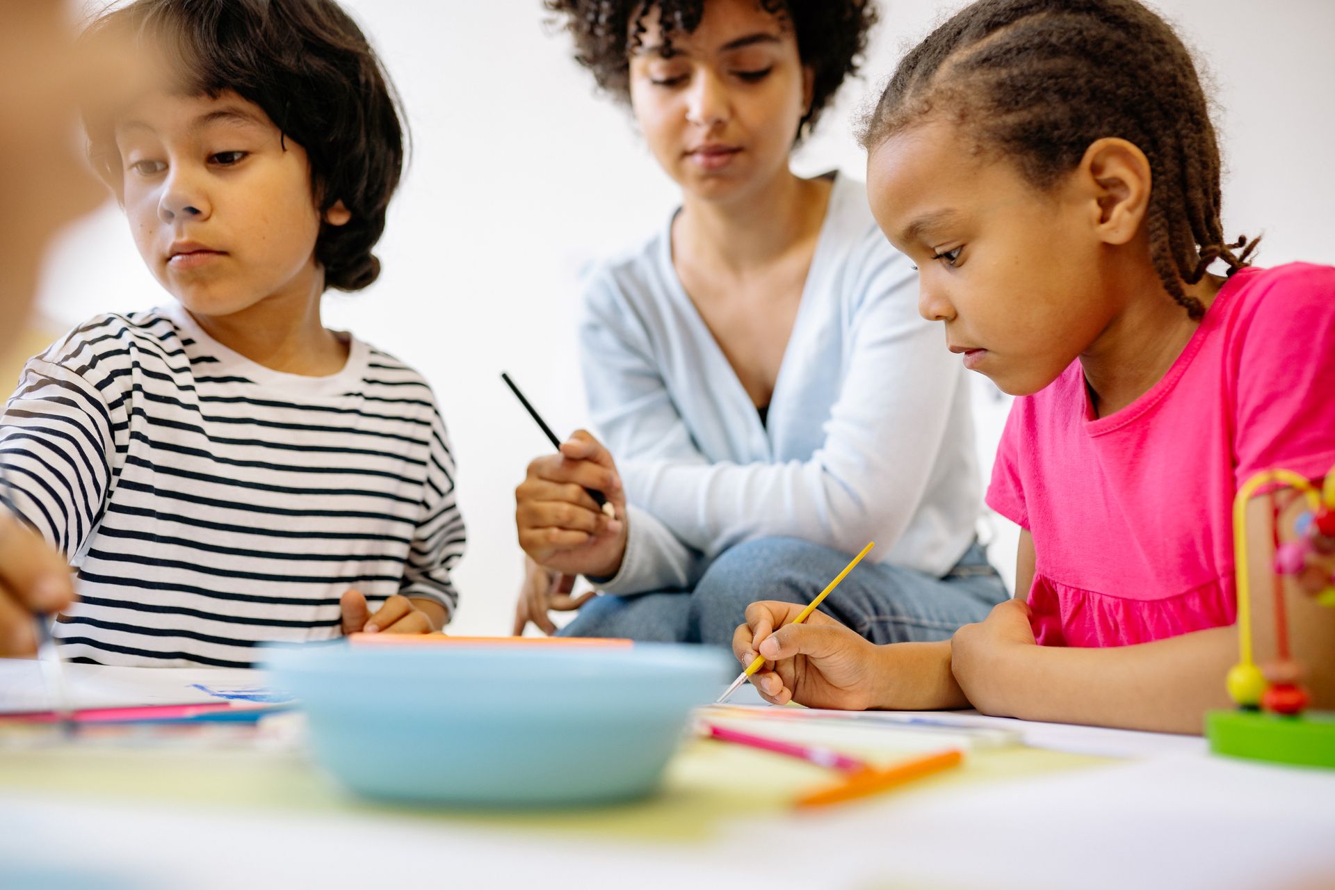 Children painting at a table with a teacher