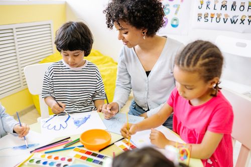 Free Children and teacher engaged in a creative painting session in a classroom setting. Stock Photo