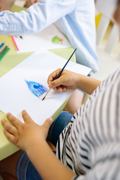 Free A young child painting with watercolors in a bright, creative classroom setting. Stock Photo