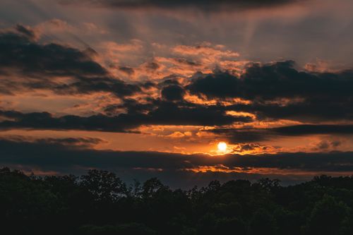 Free A stunning sunset with dramatic clouds above a silhouette of trees. Stock Photo