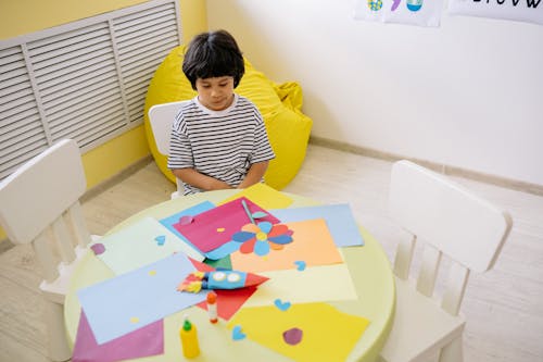 Free Boy In Striped Shirt Sitting By A Table With Art Materials Stock Photo