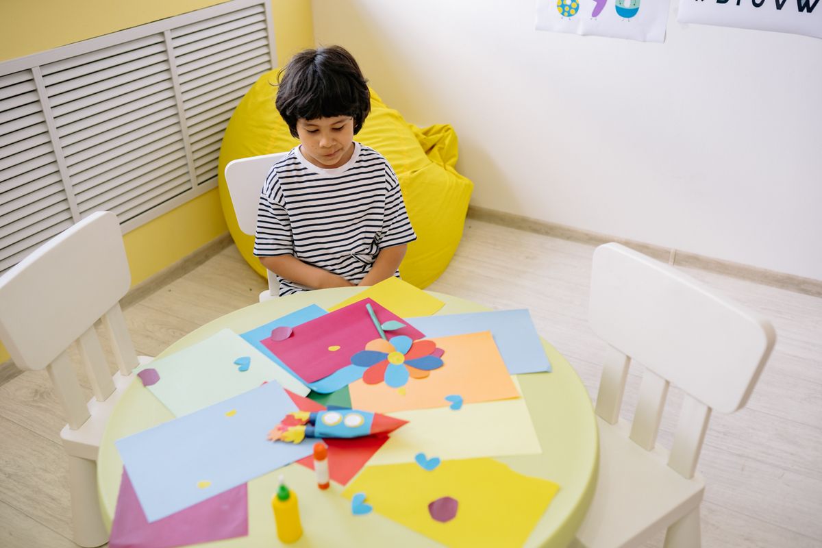 Young boy creating colorful paper crafts at a school table for paper bag puppets