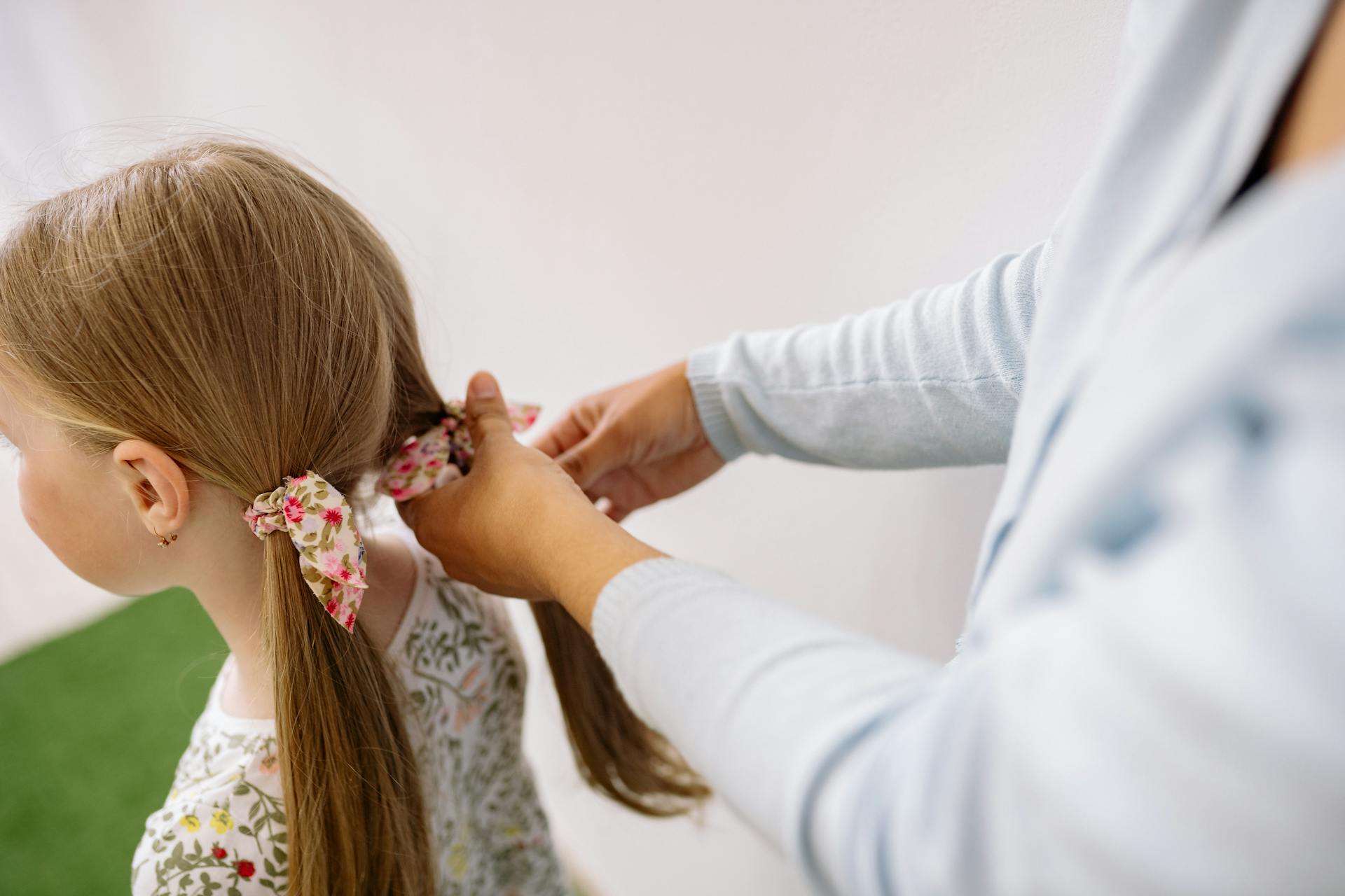 A woman styling a young girl's hair with floral hair ties indoors.