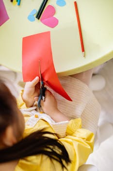Top view of a girl cutting colored paper during a creative arts and crafts session indoors.
