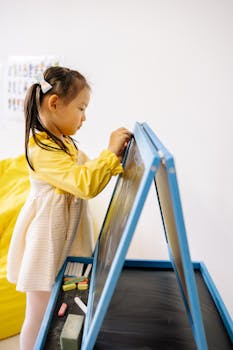 Asian child in a classroom writing on a blackboard, focusing on learning and education.