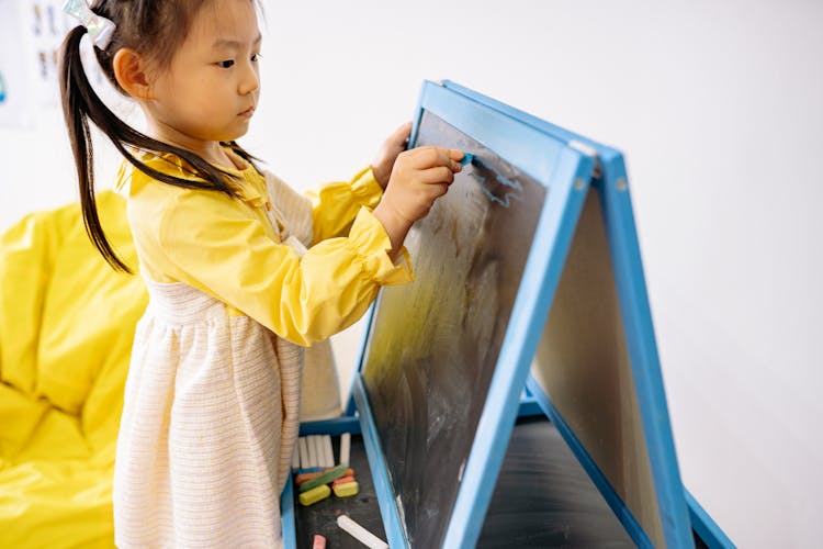 Pretty Girl In Yellow Dress Writing On A Blackboard