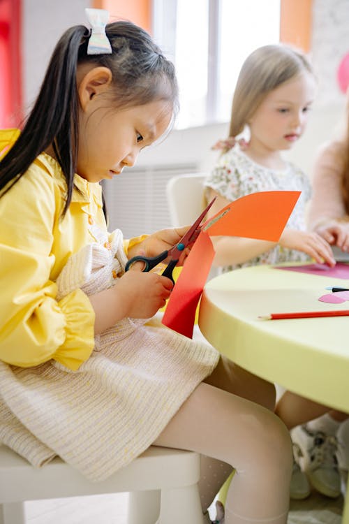 Girl In Yellow and White Dress Cutting A Colored Paper