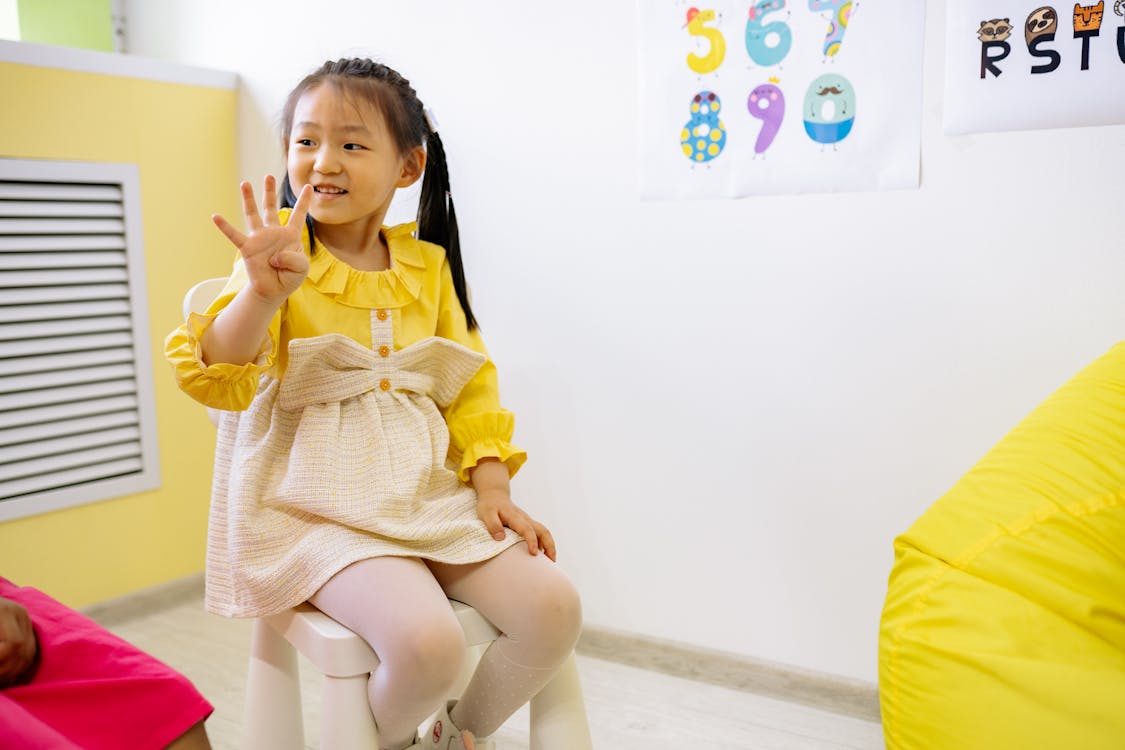 Girl in Yellow and White Dress Learning To Count With Her Fingers