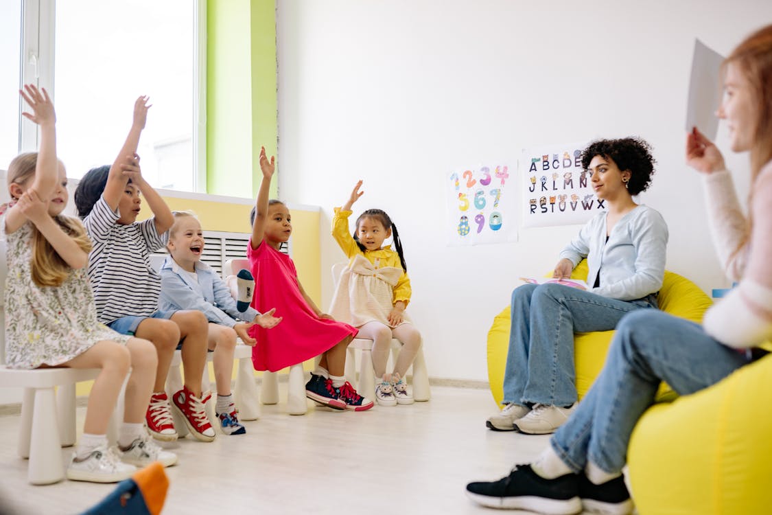 Free Children Raising Their Hands in a Classroom Stock Photo