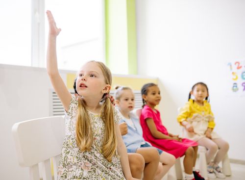 Free Kindergarten students in a classroom raising hands to participate in learning activities. Stock Photo