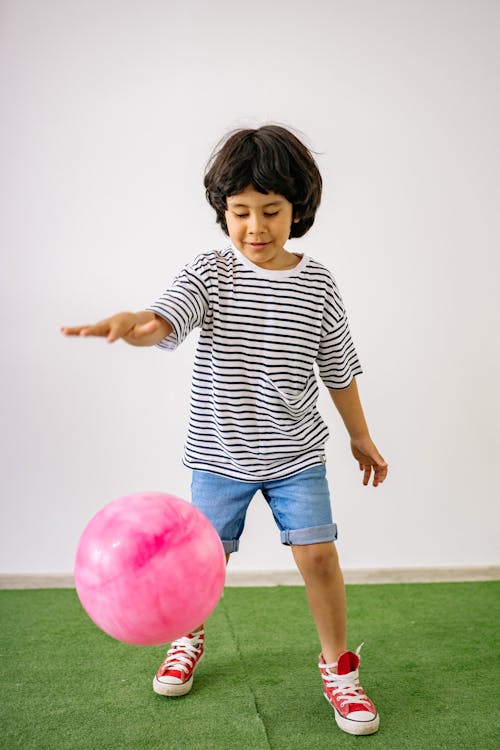 Boy in Black and White Striped Crew Neck T-shirt and Blue Denim Shorts Playing With A Pink Balloon