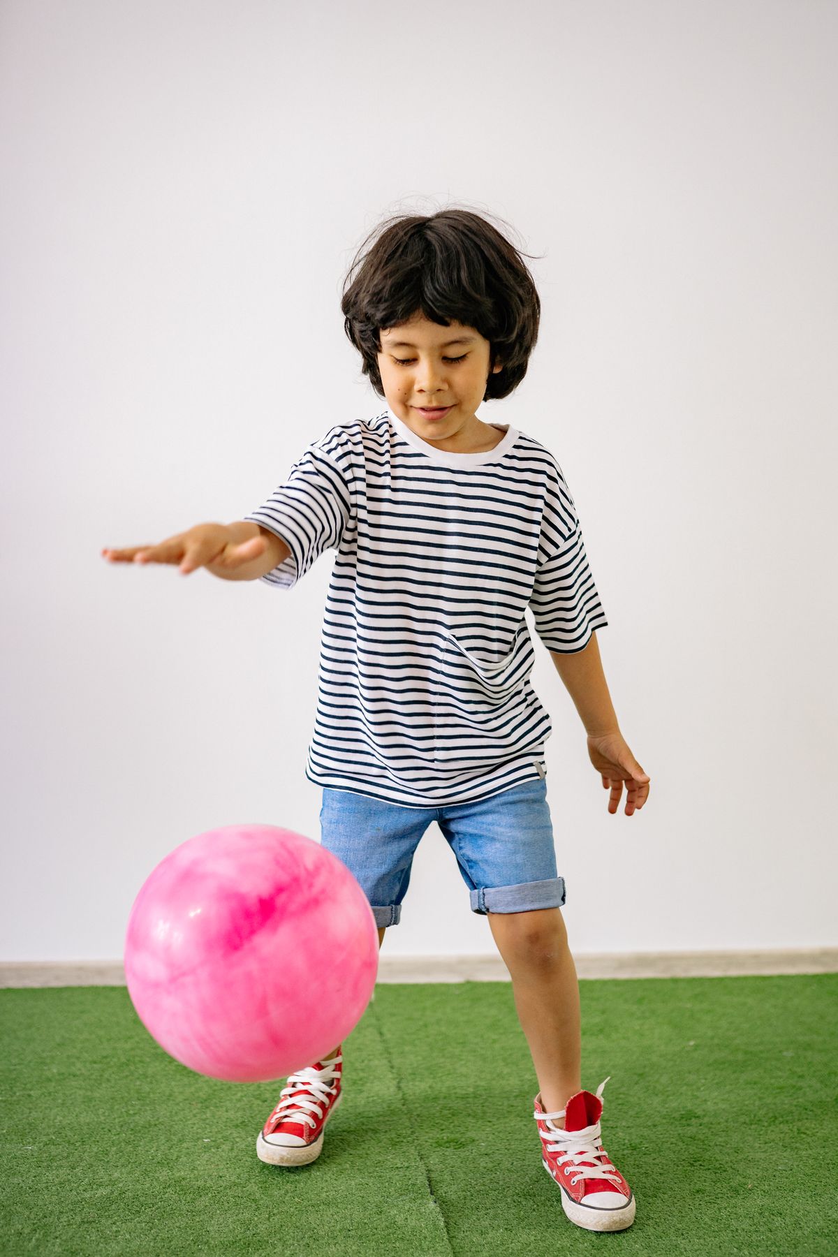 Child kicking a pink ball on a green mat.