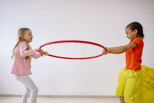 Free Two children joyfully playing with a hula hoop indoors, sharing laughter and fun. Stock Photo