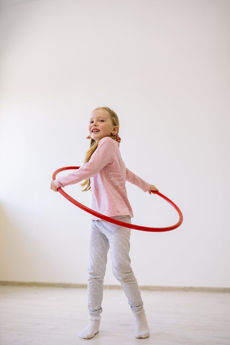 Girl In Pink Long Sleeve Shirt And White Pants Playing With A Hula Hoop