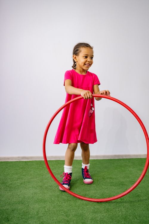 Free Smiling girl in pink dress playing with a hula hoop indoors, capturing joy and motion. Stock Photo