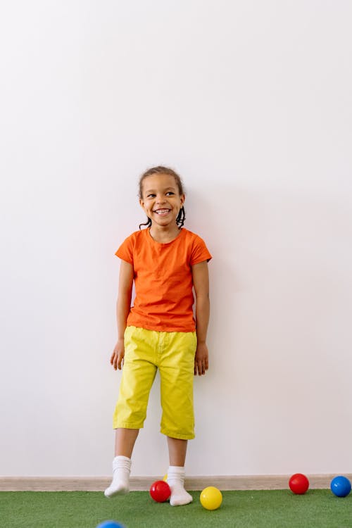 Free Smiling Girl In Orange Shirt And Yellow Pants With Braided Hair Stock Photo