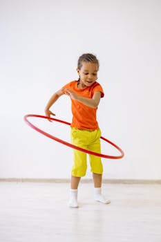 Little Girl In Orange Shirt And Yellow Pants Playing With Hula Hoop