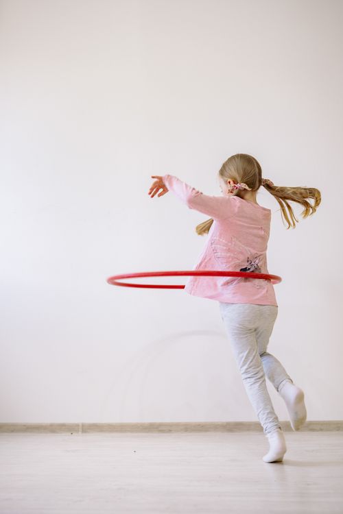 Free A young girl joyfully spins a red hula hoop in a minimalist indoor setting. Stock Photo