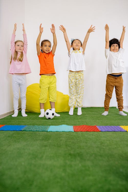 Active Children Standing On Green Carpet With Hands Raisede