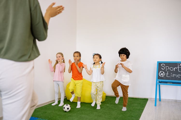 Children Playing With Their Teacher On Green Carpet