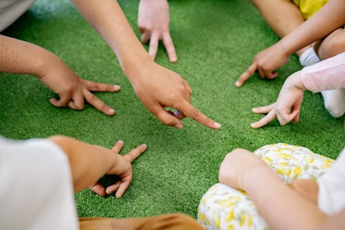 Free Children Playing With Fingers on Green Carpet Stock Photo