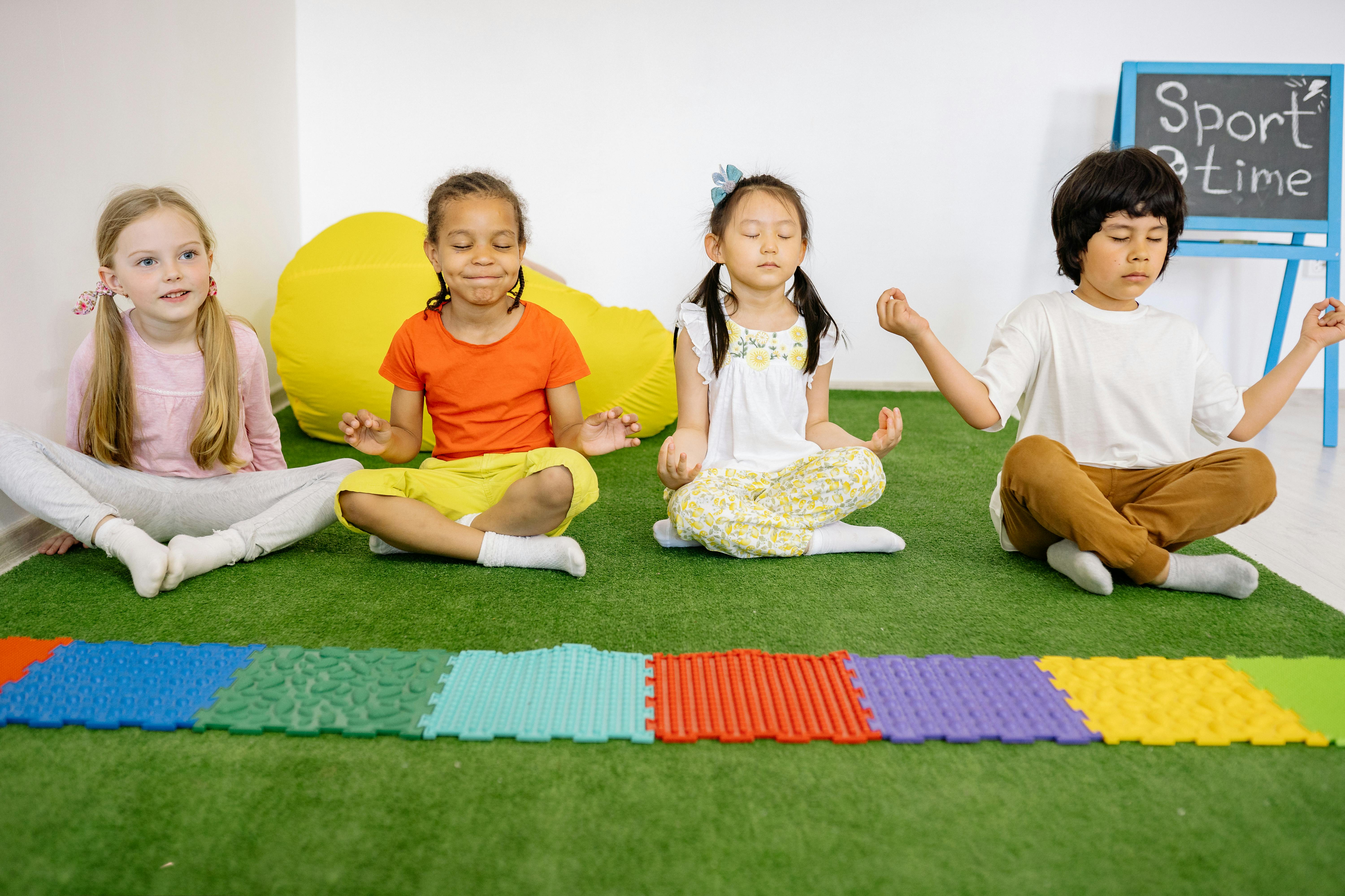 children sitting on green mat in yoga position